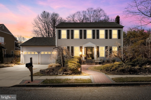 colonial-style house featuring a garage, driveway, a chimney, and fence