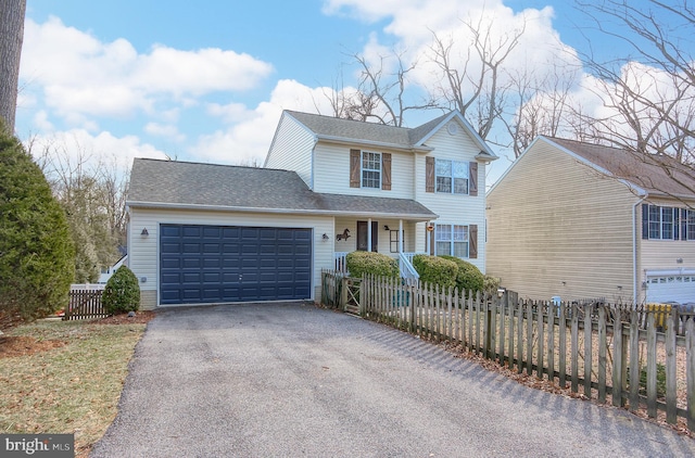 traditional-style home featuring driveway, a shingled roof, a fenced front yard, and an attached garage