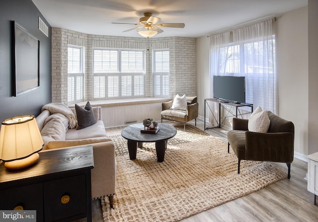 living area featuring a ceiling fan, visible vents, brick wall, and wood finished floors