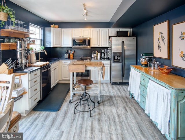 kitchen with stainless steel appliances, light wood finished floors, a sink, and white cabinetry