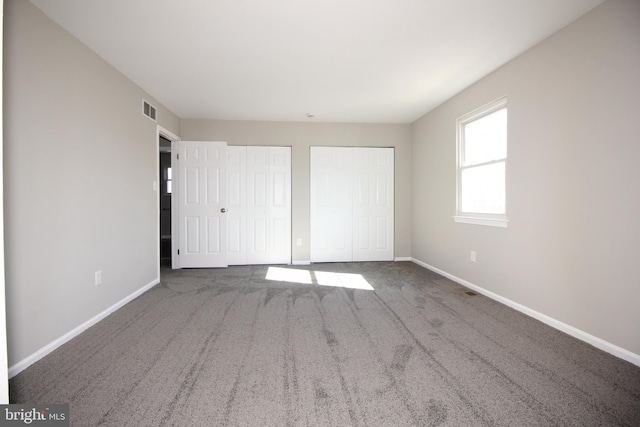 unfurnished bedroom featuring carpet, visible vents, baseboards, and two closets