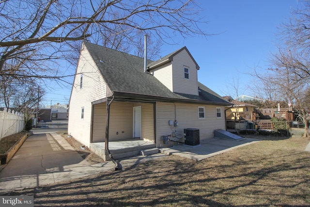 rear view of house with a shingled roof, central AC unit, a patio, fence, and a yard