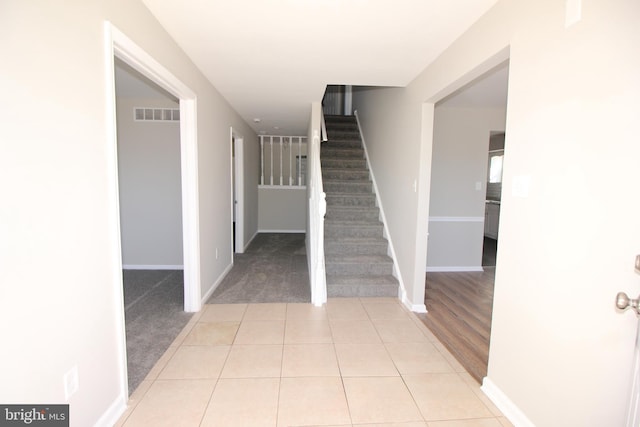 foyer entrance featuring light tile patterned flooring, light colored carpet, visible vents, baseboards, and stairs