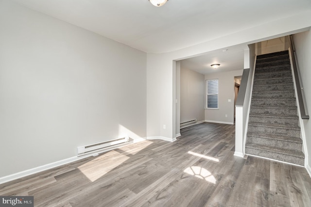 empty room featuring a baseboard radiator, stairway, and wood finished floors