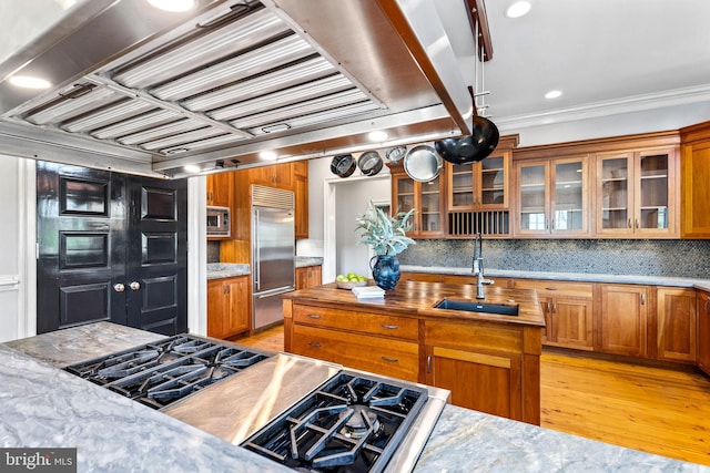 kitchen with brown cabinets, light wood-style flooring, built in appliances, and a sink