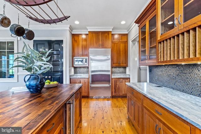 kitchen featuring butcher block counters, brown cabinetry, built in appliances, and light wood-type flooring