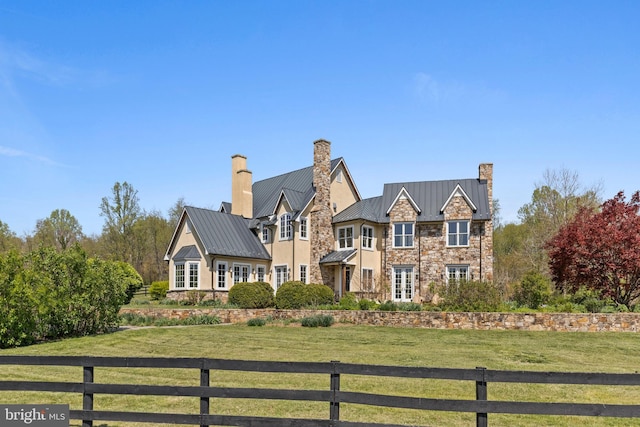 shingle-style home featuring a chimney, stone siding, fence, metal roof, and a standing seam roof