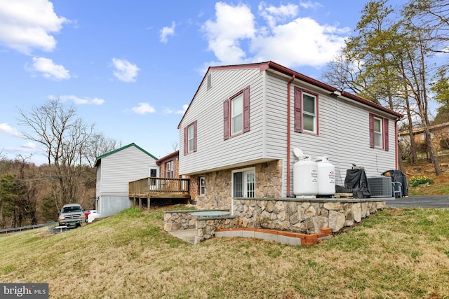 rear view of house featuring stone siding, a lawn, and a deck