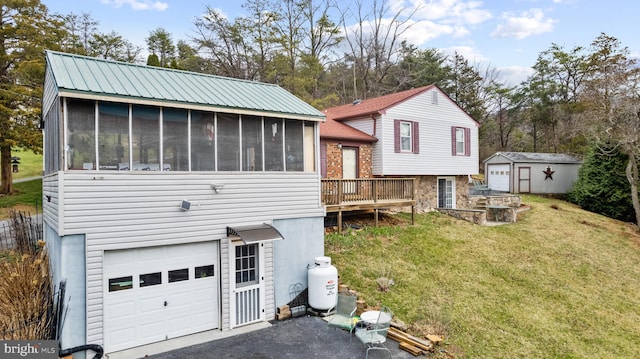 back of house featuring a sunroom, driveway, an outdoor structure, a yard, and an attached garage