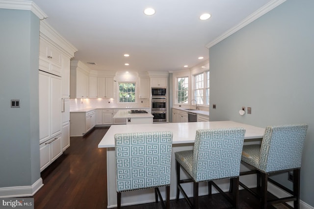 kitchen with dark wood-style flooring, stainless steel appliances, light countertops, decorative backsplash, and ornamental molding