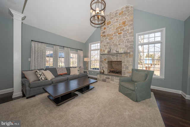 living room featuring high vaulted ceiling, a stone fireplace, wood finished floors, baseboards, and decorative columns