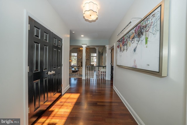 corridor with baseboards, ornate columns, and wood finished floors