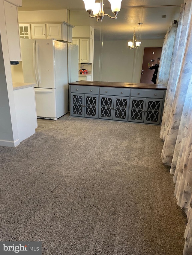 interior space with a chandelier, light carpet, white cabinets, hanging light fixtures, and freestanding refrigerator