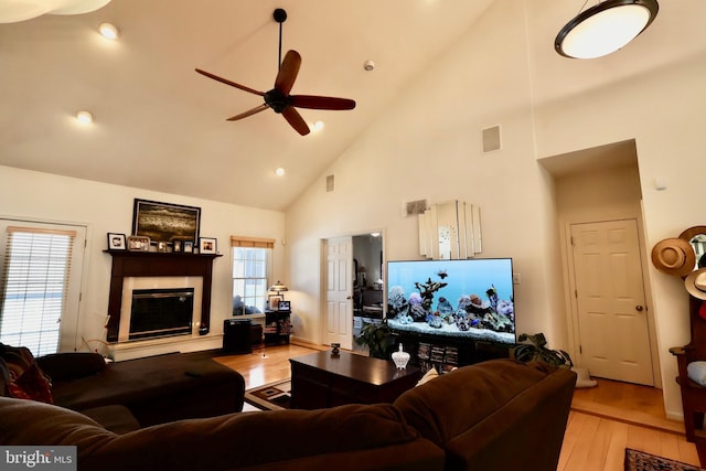 living room with visible vents, high vaulted ceiling, ceiling fan, a tile fireplace, and light wood-type flooring