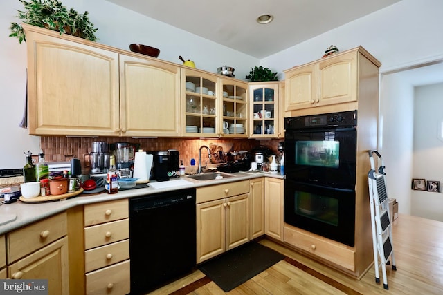 kitchen with black appliances, light brown cabinetry, a sink, light wood finished floors, and glass insert cabinets