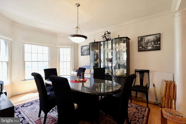 dining area featuring wood finished floors, crown molding, and ornate columns