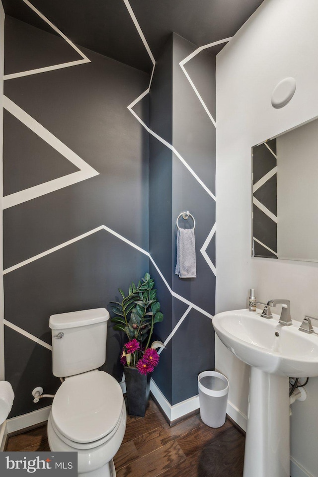 half bath featuring a sink, baseboards, toilet, and wood finished floors