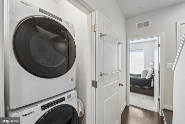 washroom with visible vents, dark wood-style flooring, stacked washer / drying machine, and laundry area