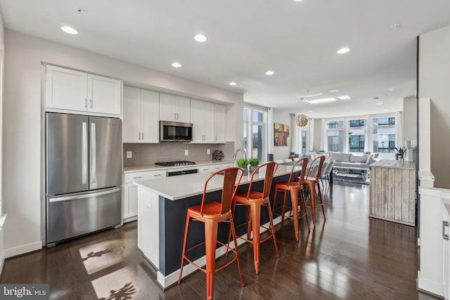 kitchen with a kitchen island with sink, light countertops, dark wood-type flooring, and appliances with stainless steel finishes