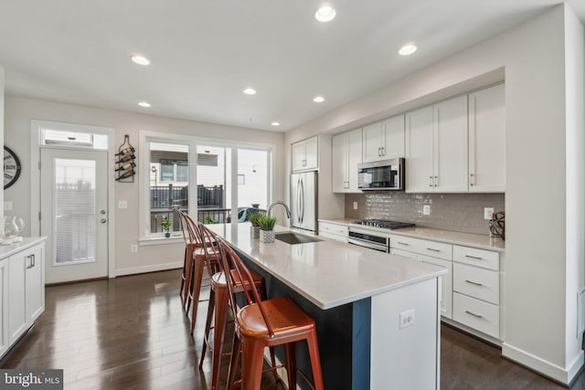 kitchen featuring tasteful backsplash, an island with sink, dark wood-style floors, stainless steel appliances, and a sink