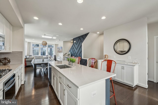 kitchen featuring decorative backsplash, appliances with stainless steel finishes, a kitchen breakfast bar, dark wood-style floors, and a sink