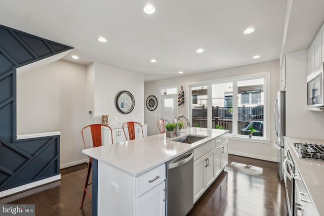 kitchen featuring a kitchen island with sink, a sink, dark wood-style floors, white cabinetry, and appliances with stainless steel finishes