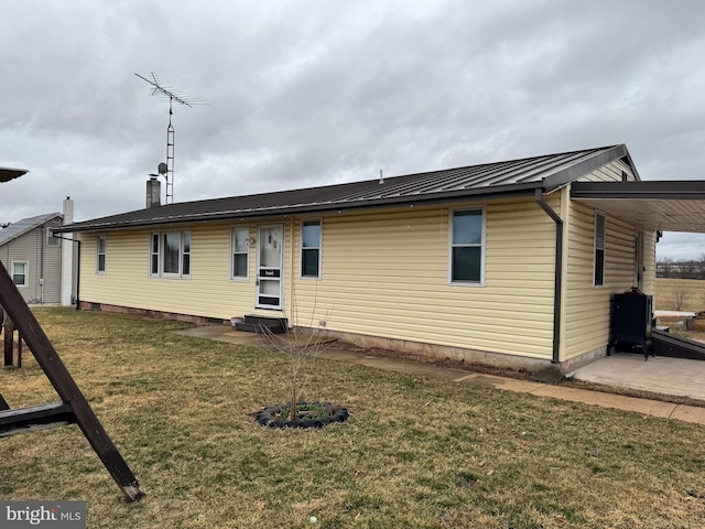 back of house with entry steps, metal roof, an attached carport, a lawn, and a standing seam roof