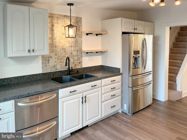 kitchen with light wood finished floors, dark countertops, stainless steel appliances, open shelves, and a sink