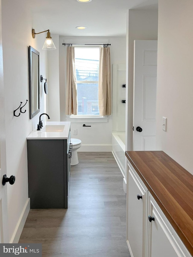 bathroom with baseboards, toilet, wood finished floors, a bathtub, and vanity