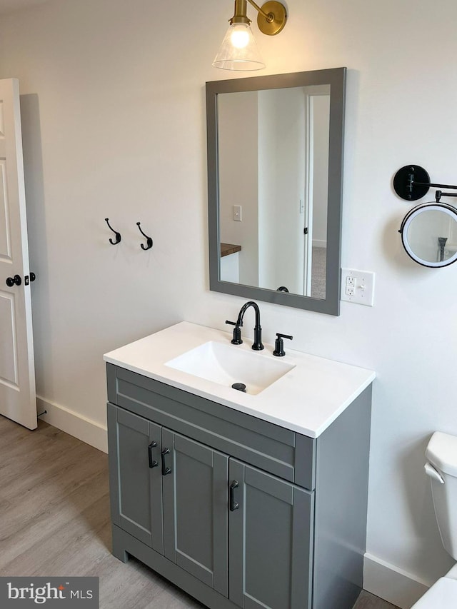 half bathroom featuring baseboards, vanity, toilet, and wood finished floors