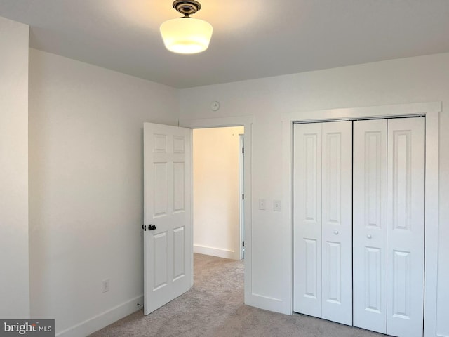 unfurnished bedroom with a closet, light colored carpet, and baseboards