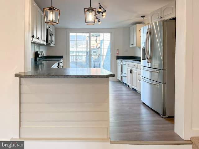 kitchen featuring stainless steel appliances, a peninsula, dark wood-style flooring, dark countertops, and decorative light fixtures