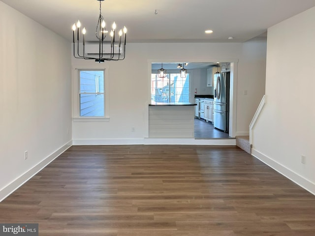 unfurnished dining area with baseboards, a chandelier, and dark wood-style flooring