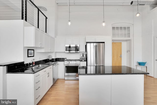 kitchen with appliances with stainless steel finishes, a sink, a high ceiling, and light wood-style floors