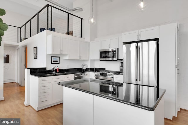 kitchen with stainless steel appliances, light wood-style floors, a sink, and a towering ceiling