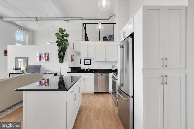 kitchen with stainless steel appliances, dark countertops, open floor plan, white cabinetry, and a sink