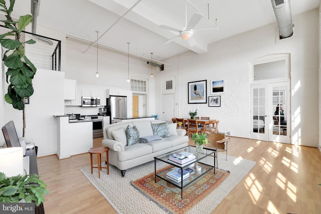 living area with a towering ceiling, light wood finished floors, ceiling fan, and french doors