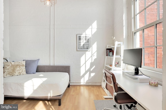 bedroom featuring light wood finished floors, brick wall, and multiple windows