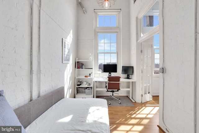 office space featuring brick wall, plenty of natural light, a high ceiling, and wood finished floors