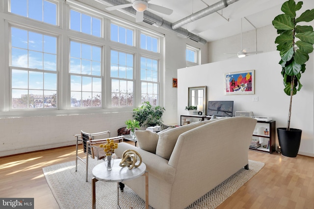 living area with ceiling fan, light wood finished floors, and a high ceiling