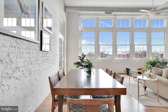 dining space featuring brick wall, visible vents, ceiling fan, and wood finished floors