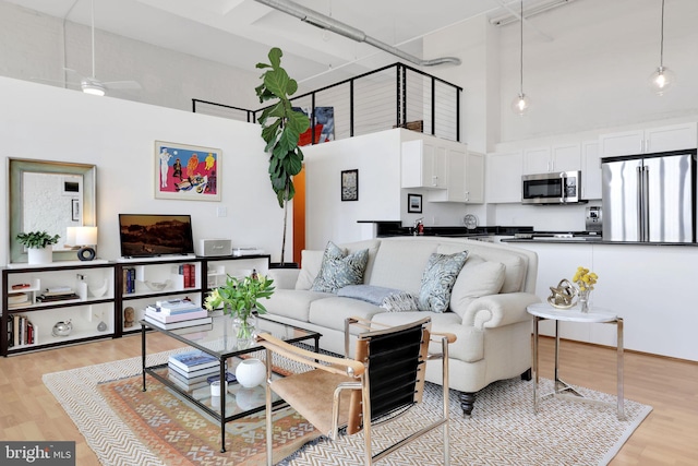 living room featuring light wood-style floors, a high ceiling, and a ceiling fan