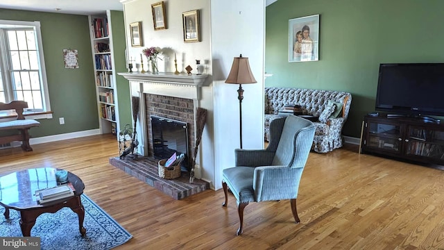 living area with baseboards, a brick fireplace, and wood finished floors