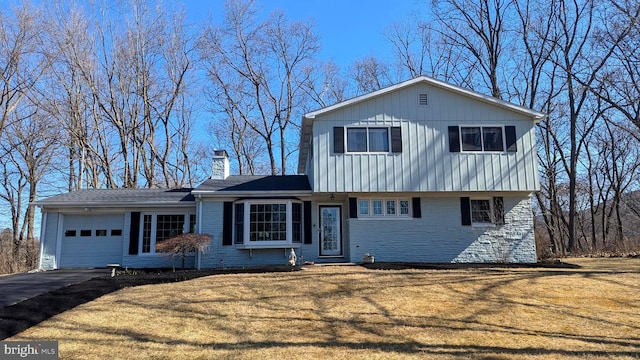 view of front of house featuring aphalt driveway, an attached garage, a front yard, brick siding, and a chimney