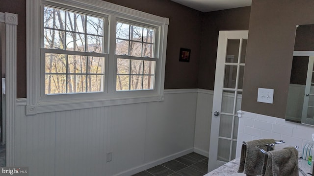 entryway featuring dark tile patterned floors, a healthy amount of sunlight, and wainscoting