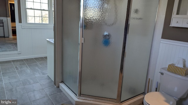 bathroom featuring a wainscoted wall, toilet, and a stall shower