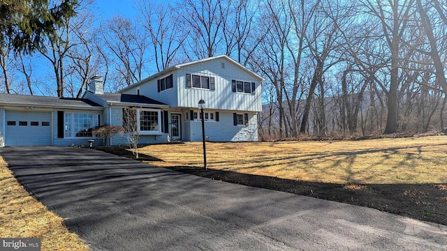 view of front of home featuring a chimney, a front lawn, a garage, aphalt driveway, and brick siding