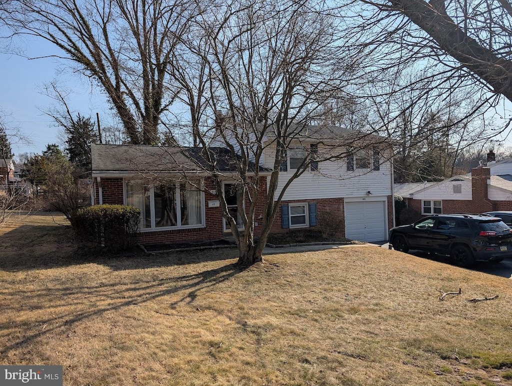 tri-level home with brick siding, an attached garage, and a front lawn