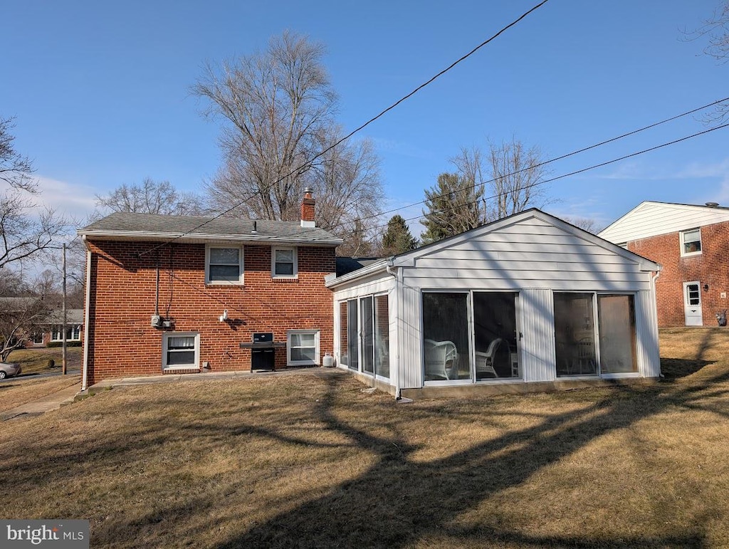 back of house with a yard, brick siding, and a sunroom