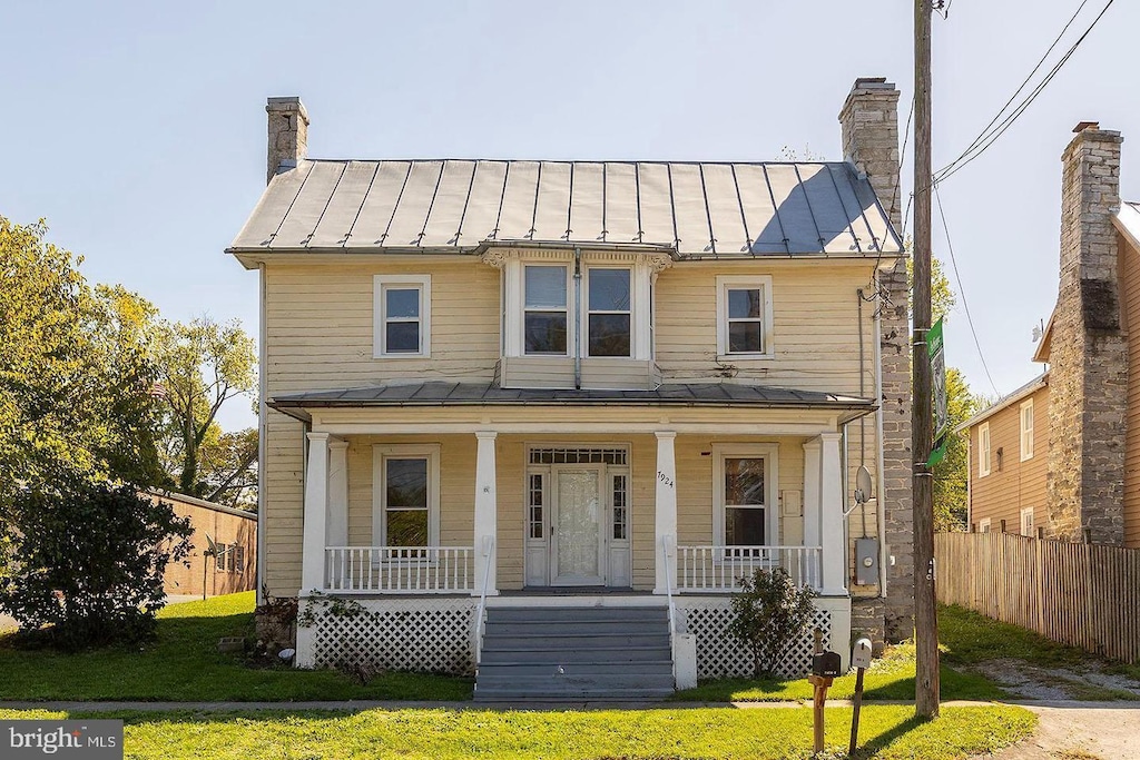 view of front of property featuring metal roof, a standing seam roof, a chimney, and a porch